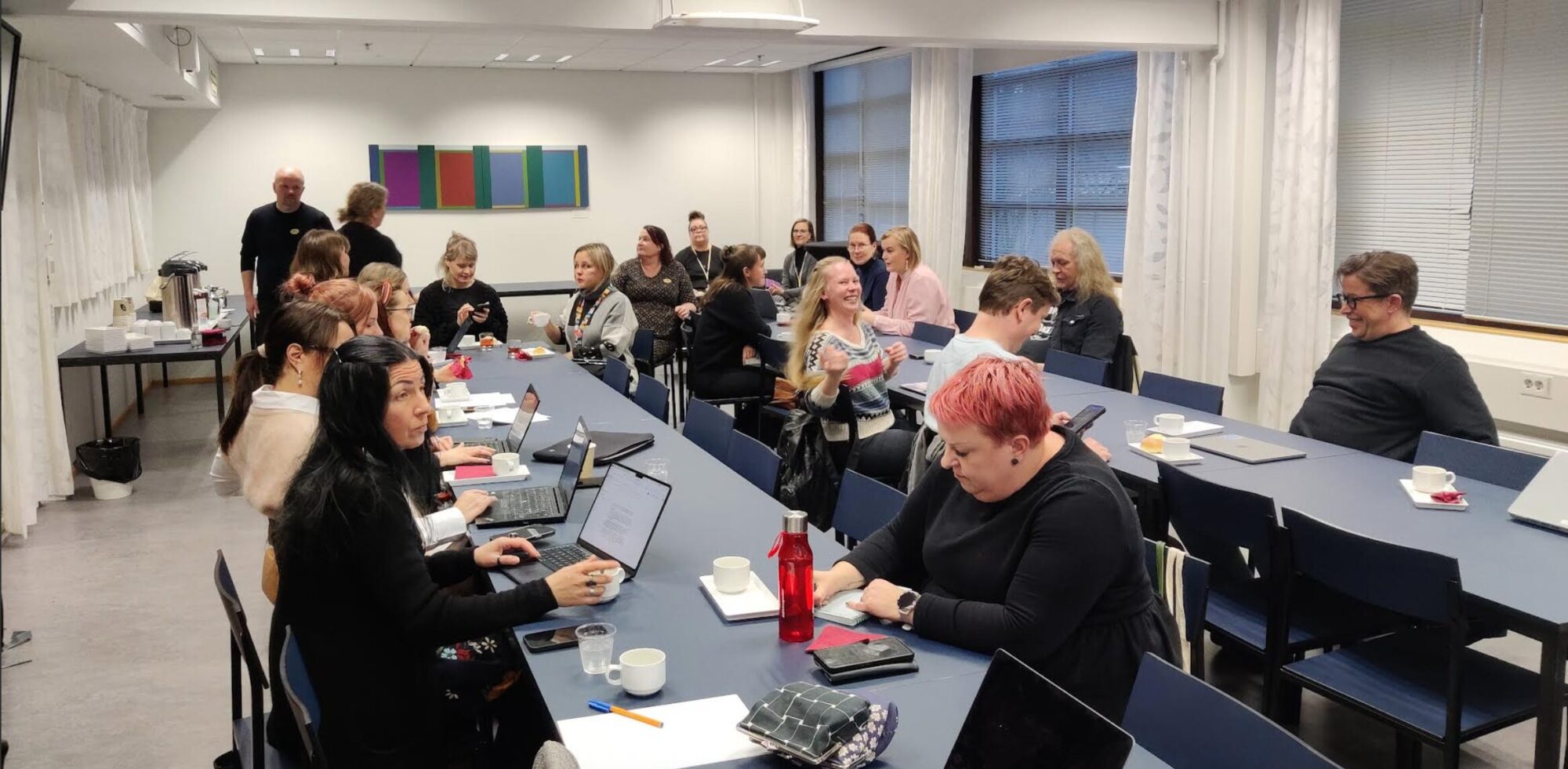 Ihmiset istuvat ja kuuntelevat tai kirjoittavat muistiinpanoja.